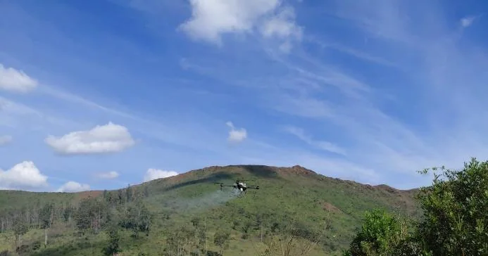 Drone agrícola em aplicação aérea sobre encosta em recuperação